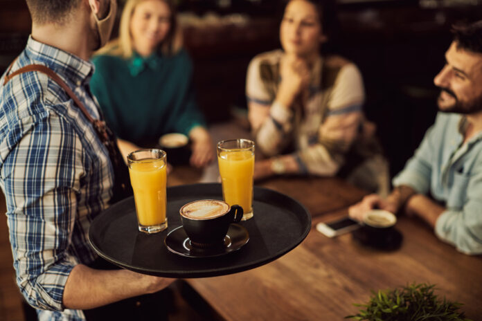 Close-up of waiter serving drinks to customers in a cafe.